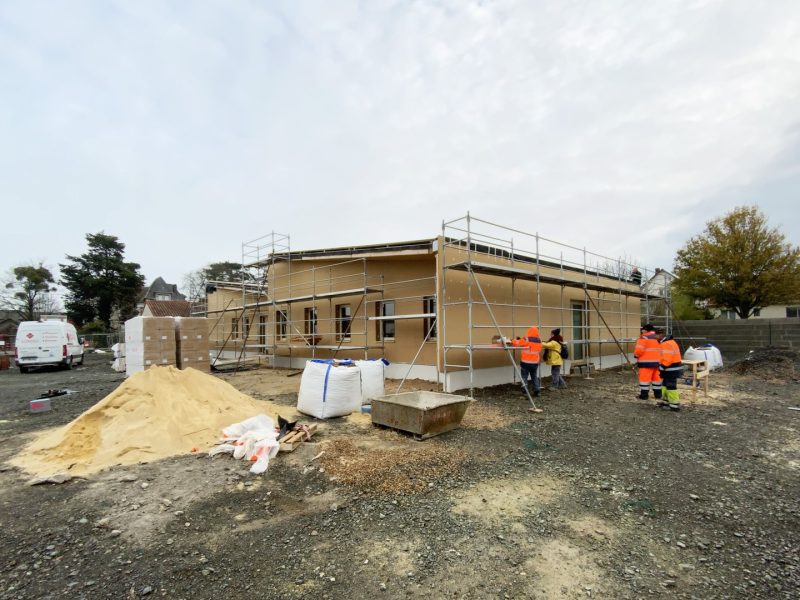 Construction d'une maison individuelle en bois avec échafaudage, ouvriers sur chantier, matériaux et engins