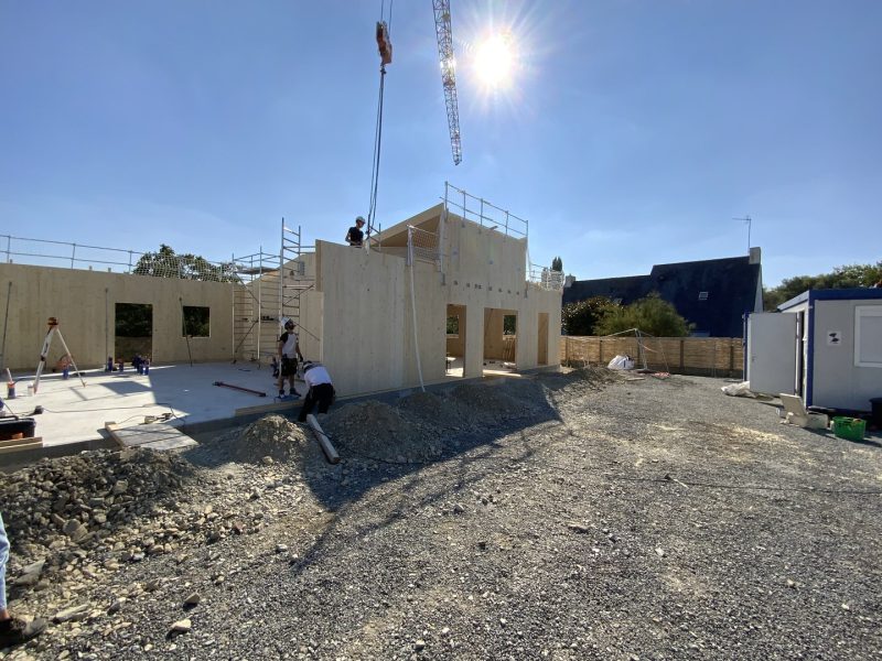 Construction d'une maison en panneaux bois préfabriqués avec grue, fondations en béton et gravier sur le chantier