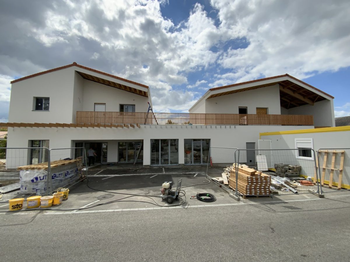 Bâtiment commercial en construction, façades blanches, toiture tuiles rouges, balcon bois, chantier en cours