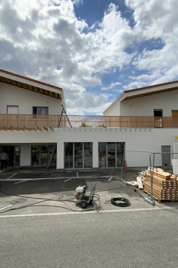 Bâtiment commercial en construction, façades blanches, toiture tuiles rouges, balcon bois, chantier en cours