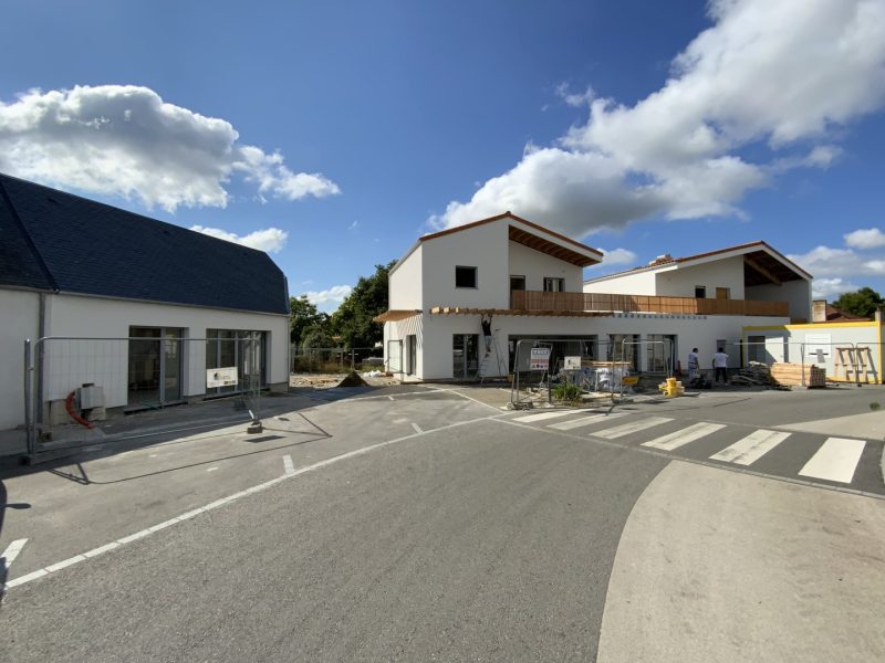 Ensemble de maisons contemporaines en construction avec bardage bois et enduit blanc, toitures asymétriques, parking et passage piéton