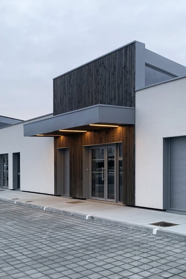 Ensemble de bâtiments modernes avec bardage bois vertical, façades blanches et volets roulants sur parking pavé