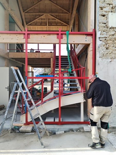 Structure métallique rouge dans une grange en rénovation avec charpente bois apparente et murs en pierre