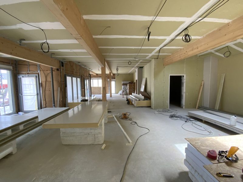 Espace intérieur en construction avec poutres bois apparentes, plafond clair, sols béton et cloisons en cours d'installation