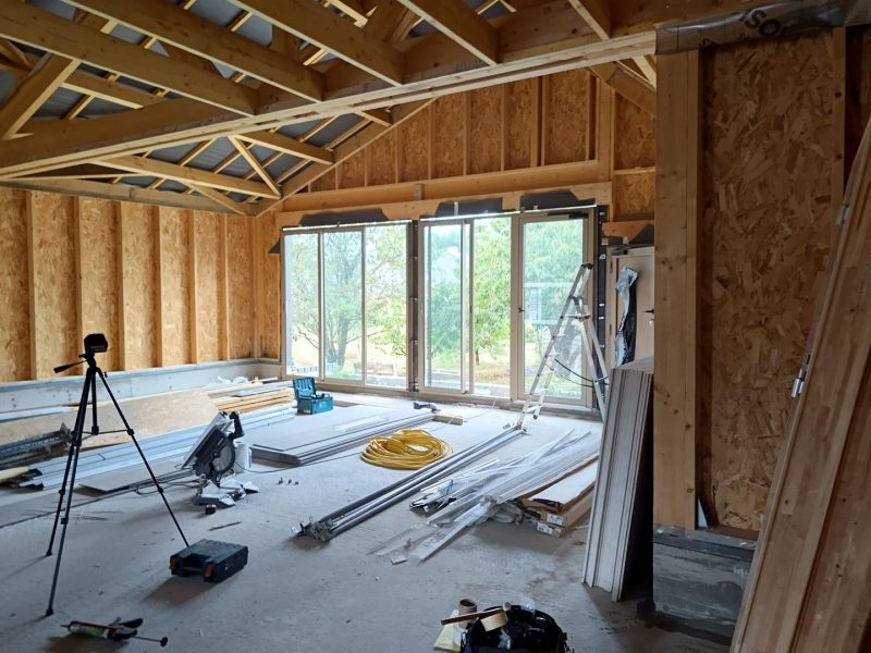 Chantier de construction intérieur avec ossature bois, baies vitrées et charpente apparente en cours d'aménagement