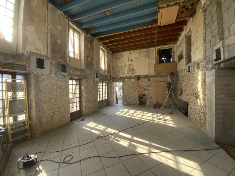 Rénovation d'un espace intérieur ancien avec murs en pierre apparente, plafond à poutres bois et carrelage au sol