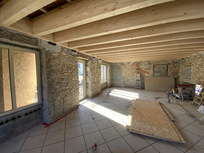 Rénovation intérieure en cours : murs en pierre apparente, plafond avec poutres bois, sol avec panneaux isolants