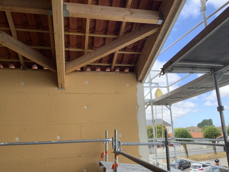 Charpente en bois apparente avec tuiles terracotta, mur isolant jaune et échafaudage lors de travaux de rénovation