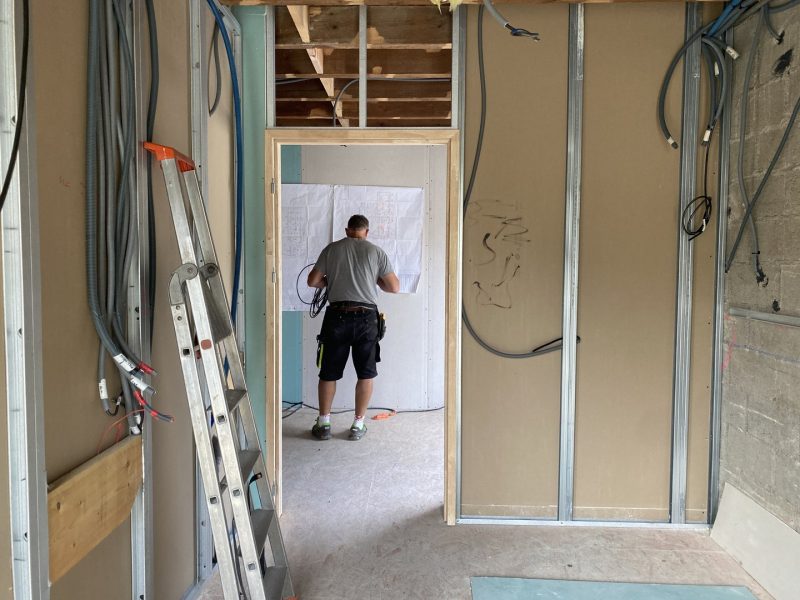 Ouvrier sur chantier de rénovation intérieure, cloisons en plaques de plâtre, échelle et câbles électriques apparents