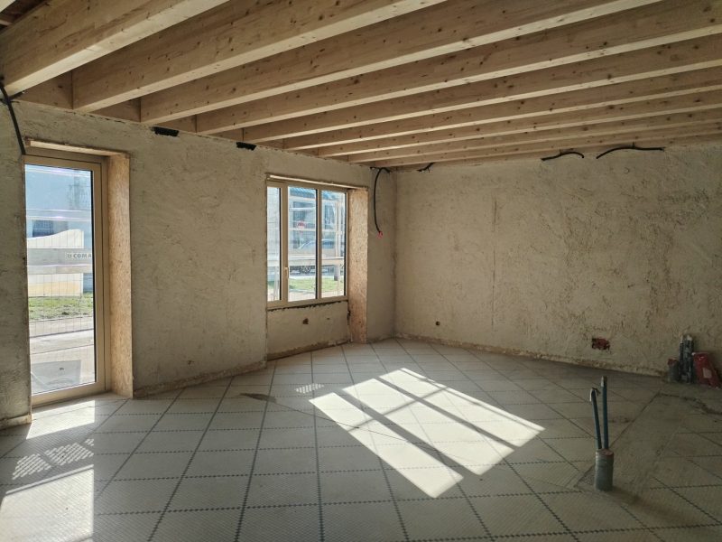 Intérieur en construction avec murs en terre crue, plafond en bois apparent et sol quadrillé