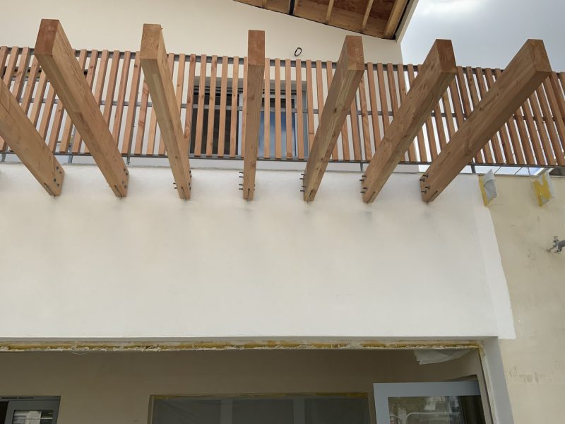 Balcon en bois avec garde-corps à barreaux verticaux et poutres diagonales apparentes sous structure
