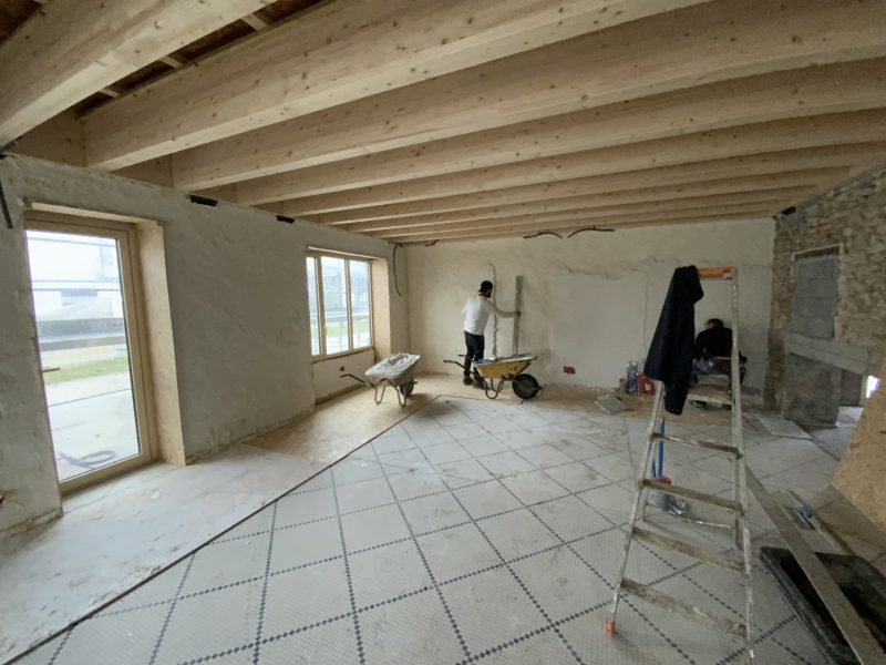 Rénovation d'un espace intérieur avec poutres en bois apparentes, murs en plâtre blanc et carrelage au sol en cours de pose