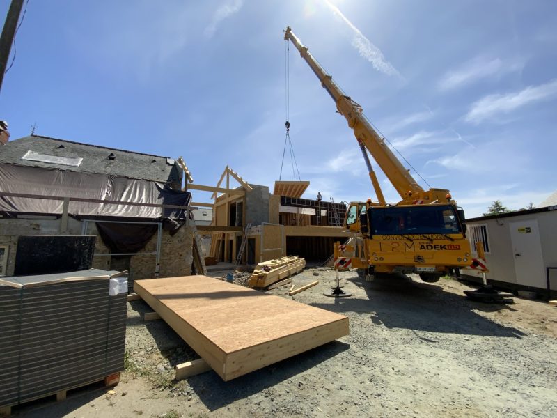 Construction d'une maison contemporaine en bois avec grue jaune soulevant des panneaux préfabriqués sur chantier