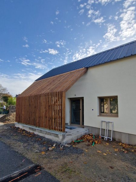 Maison contemporaine avec bardage bois vertical, enduit blanc, toit métallique bleu, en cours de finition