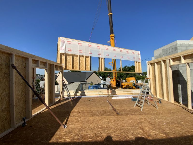 Levage d'un panneau de mur préfabriqué en bois par grue sur chantier de construction ossature bois