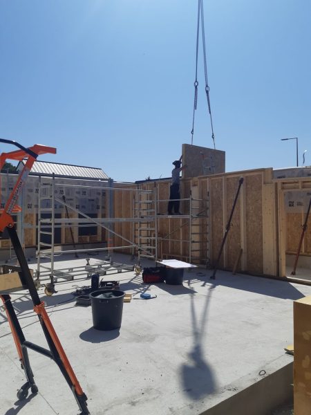 Levage d'un panneau préfabriqué en bois sur chantier de construction avec échafaudage et grue
