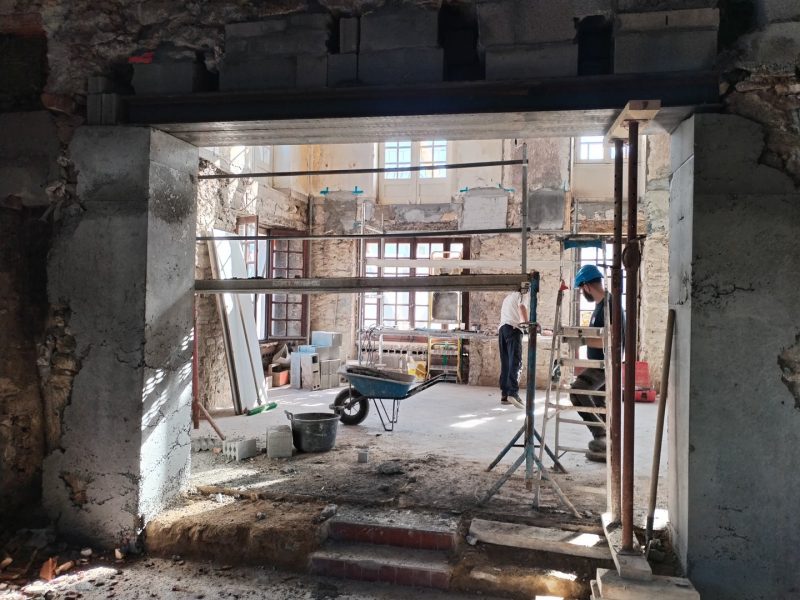 Rénovation d'un bâtiment en cours avec échafaudage, ouverture traversante encadrée béton et murs en pierre apparente
