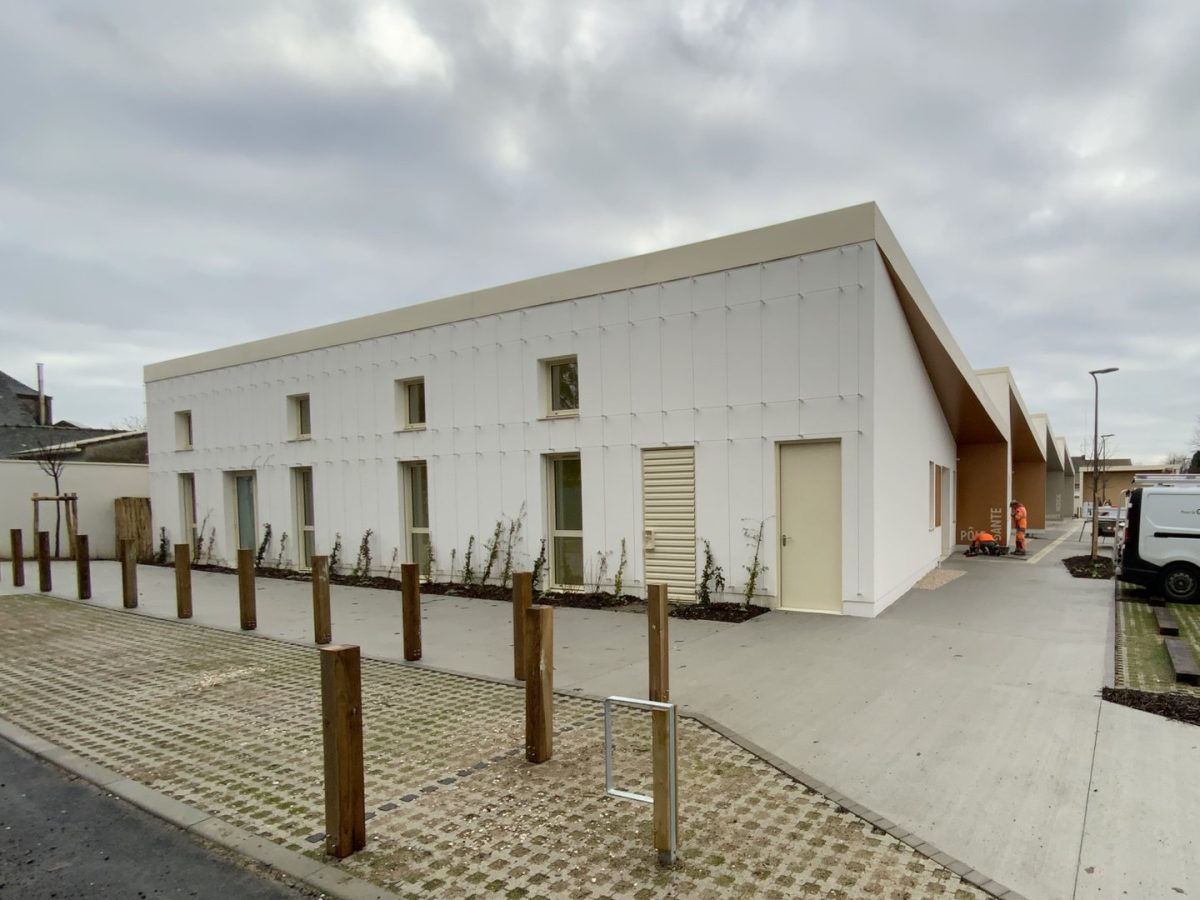 Bâtiment moderne blanc à toiture inclinée avec façade en panneaux, fenêtres régulières et poteaux bois délimitant l'espace