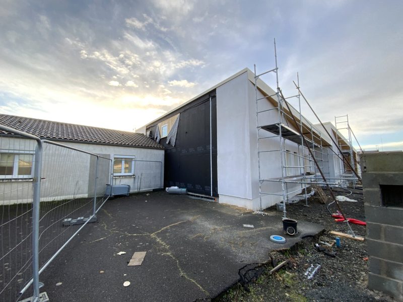 Maison en rénovation avec échafaudage, façade blanche et bardage noir, chantier en cours sous ciel nuageux