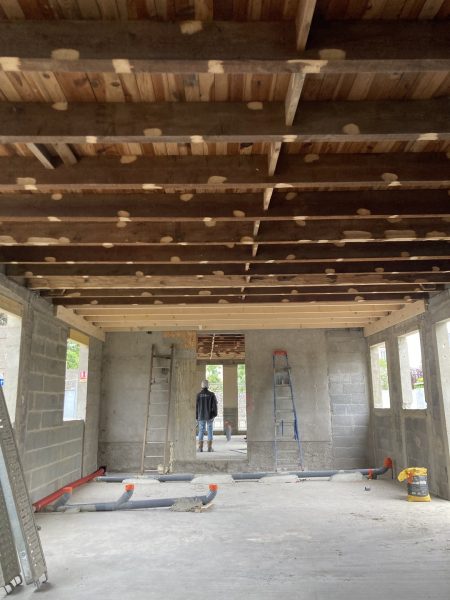 Chantier d'extension en parpaings avec charpente bois apparente, plancher béton et canalisations en attente