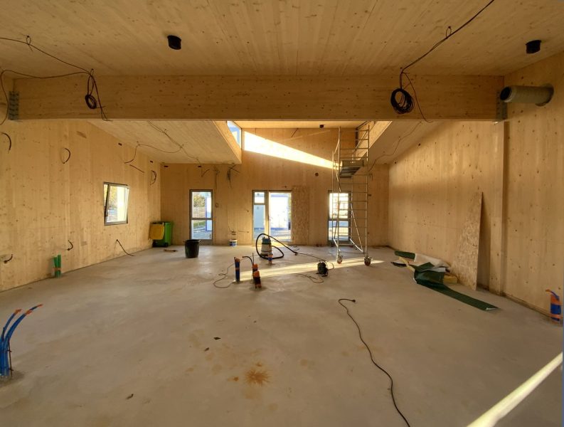 Intérieur en construction avec murs et plafond en bois clair, béton au sol, câbles électriques apparents et échelle