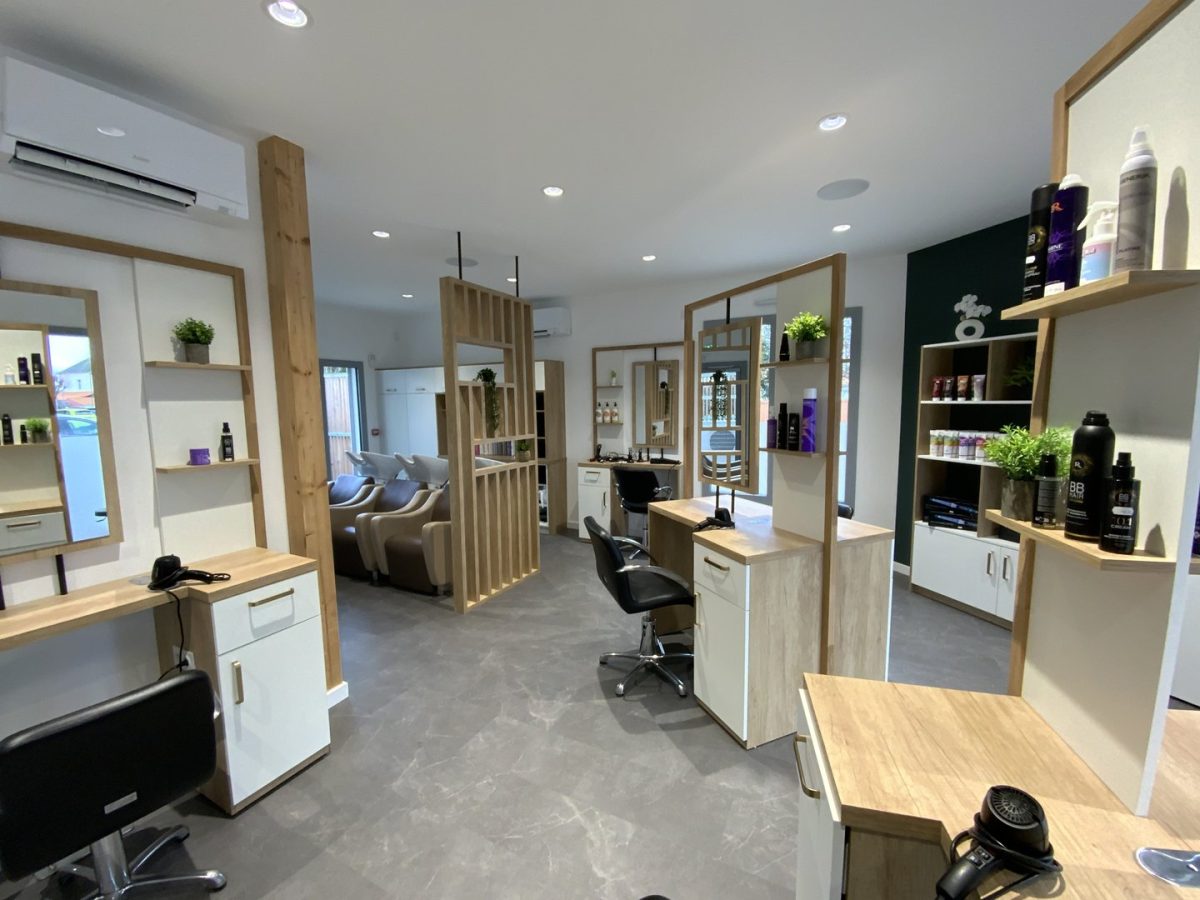 Salon de coiffure moderne avec mobilier bois clair et blanc, miroirs encadrés, étagères de produits et plafond blanc