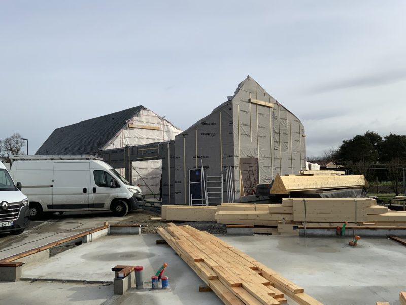 Maison en ossature bois en construction, isolation extérieure visible, chantier avec matériaux au sol