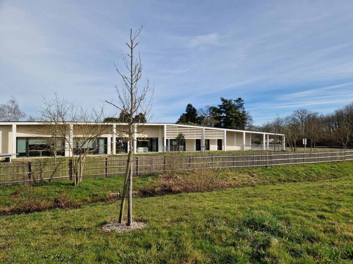 Bâtiment moderne en bois clair avec bardage horizontal, entouré d'une clôture bois et d'espaces verts avec arbres
