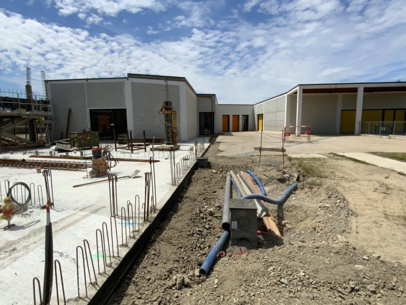 Chantier de construction d'un bâtiment moderne avec ferraillage au premier plan et structures en béton et bardage métallique