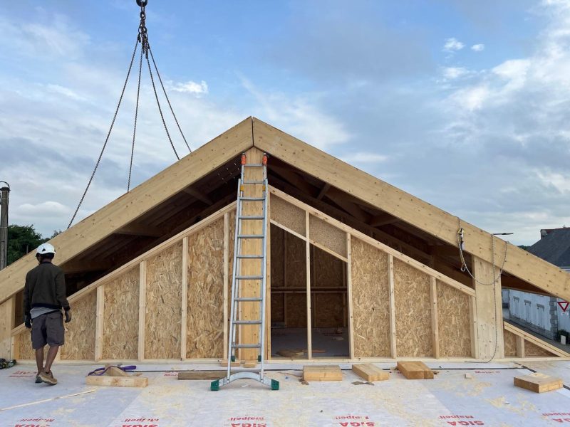 Module préfabriqué en bois avec toiture à pignon, ossature bois et panneaux OSB, en cours de levage par chaînes