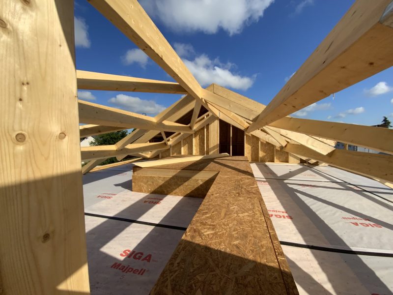 Charpente en bois massif avec fermes apparentes sur plancher OSB et isolant, ciel bleu, construction en cours