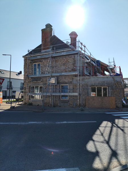 Bâtiment en pierre en rénovation avec échafaudage, cheminées en brique apparente, situé à un carrefour urbain