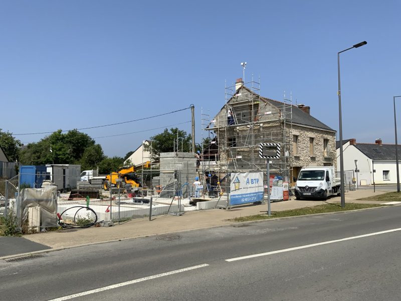 Maison en pierre en rénovation avec échafaudage, chantier de construction avec grue et matériaux, rue de village