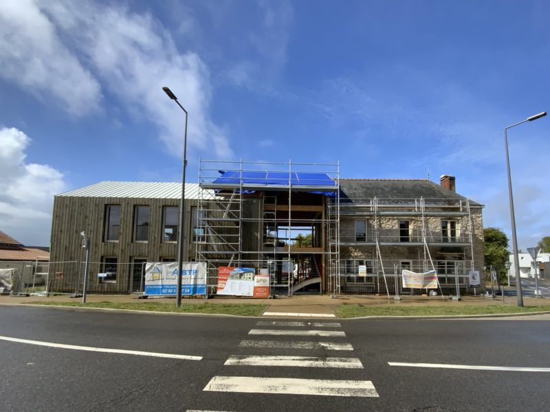 Rénovation d'un bâtiment en pierre avec extension bois moderne, échafaudages et bâches de chantier visibles