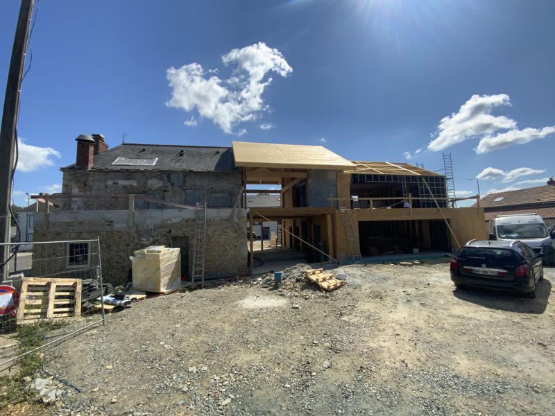 Chantier de rénovation avec ancienne bâtisse en pierre et extension moderne à ossature bois, toiture en construction