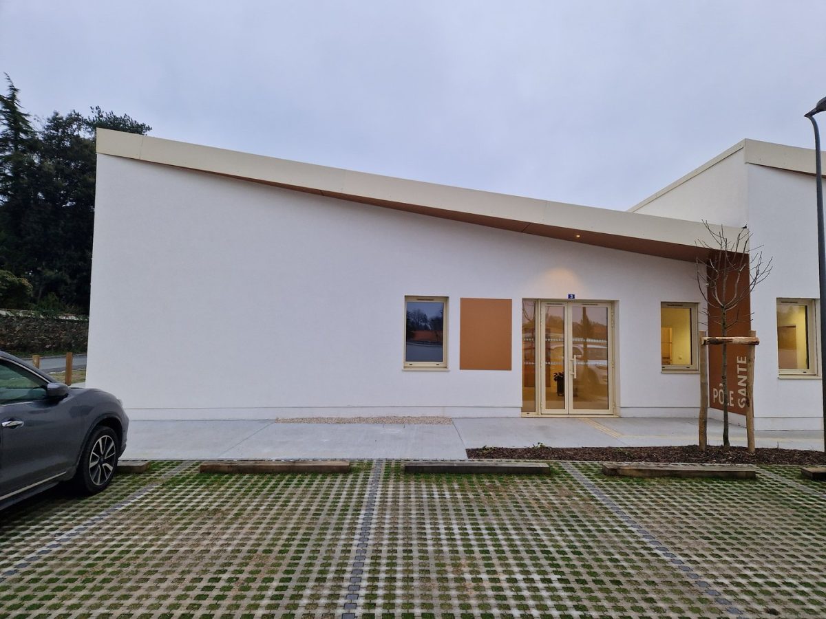 Bâtiment moderne blanc avec toiture plate, façade épurée, portes vitrées et parking écologique à dalles perméables