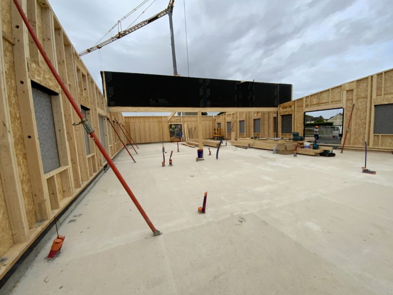 Construction d'un bâtiment à ossature bois avec murs en cours de montage, panneau noir suspendu par grue