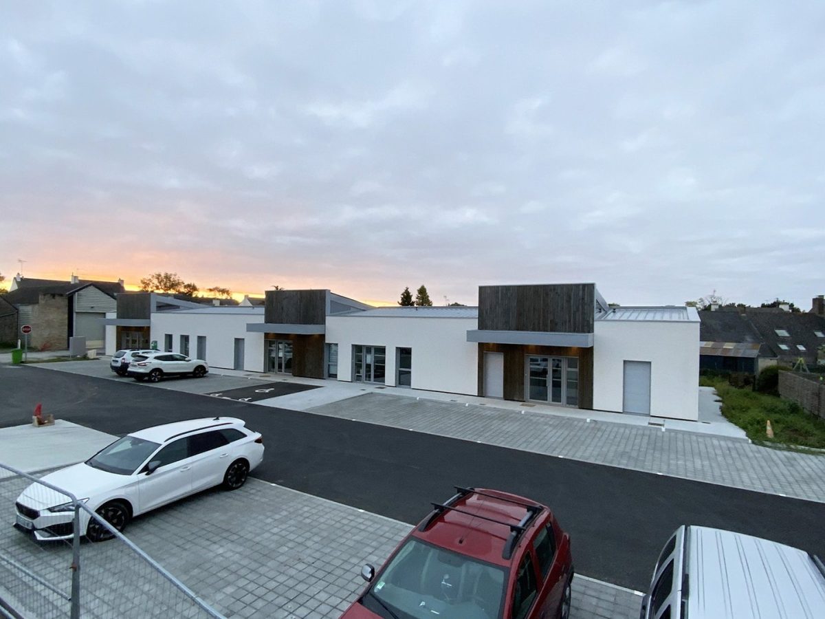 Ensemble de bâtiments commerciaux modernes blancs avec bardage bois, toitures plates et parking asphalté au crépuscule
