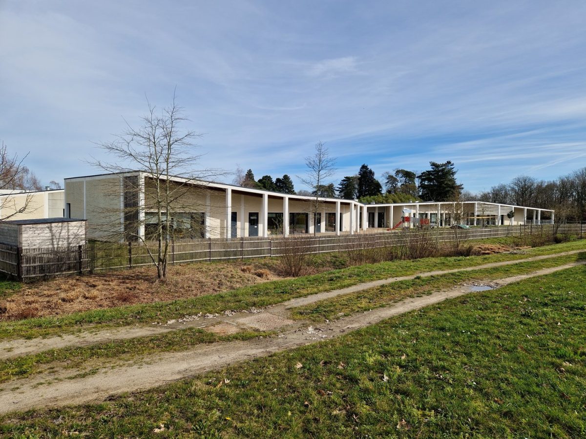 Bâtiment moderne de plain-pied en briques beiges avec colonnade blanche, entouré d'espaces verts et d'arbres