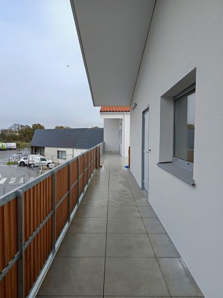 Coursive extérieure avec terrasse en carrelage beige, garde-corps bois, murs blancs et porte d'entrée moderne