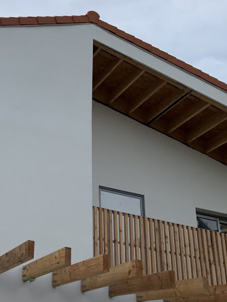 Maison contemporaine blanche avec toit en tuiles rouges, balcon en bois et débord de toiture apparent