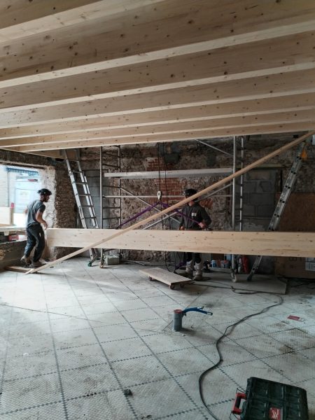 Chantier de rénovation avec structure en bois apparente, poutres au plafond et murs en pierre brute
