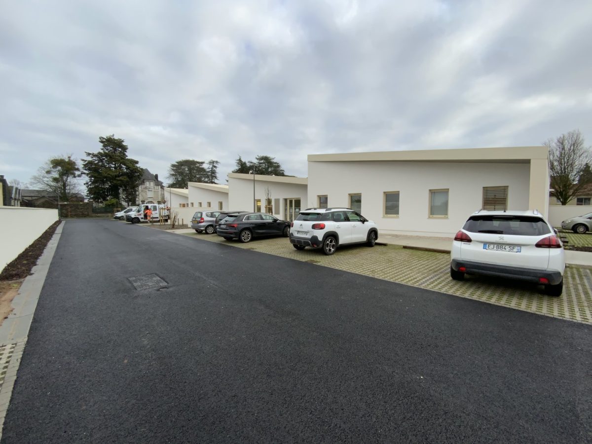 Bâtiment moderne à toiture plate avec façade blanche, parking avec grille stabilisatrice et véhicules garés