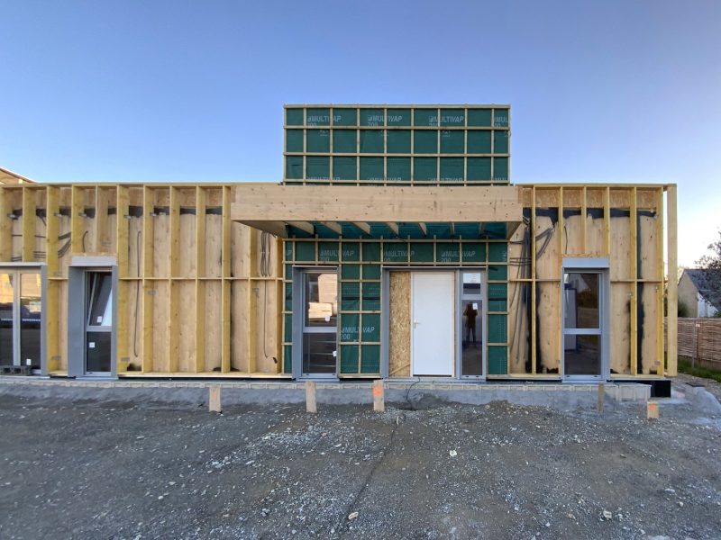 Maison individuelle en construction avec ossature bois apparente et panneaux isolants verts, sur dalle béton