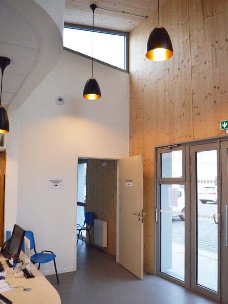 Hall d'accueil lumineux avec plafond bois, murs blancs, suspensions design noires et portes vitrées