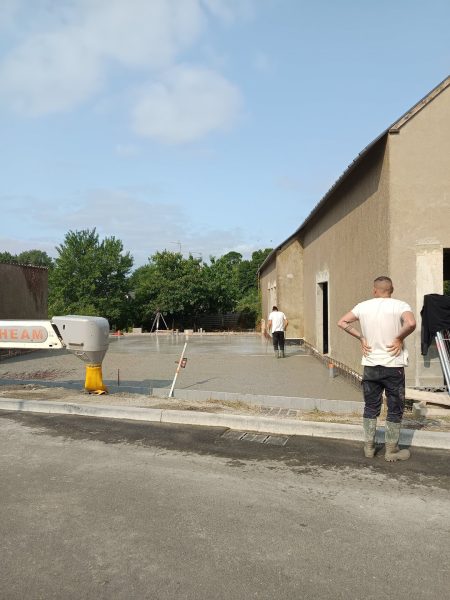 Dalle béton fraîchement coulée devant bâtiment enduit beige avec camion toupie et ouvriers sur chantier de construction
