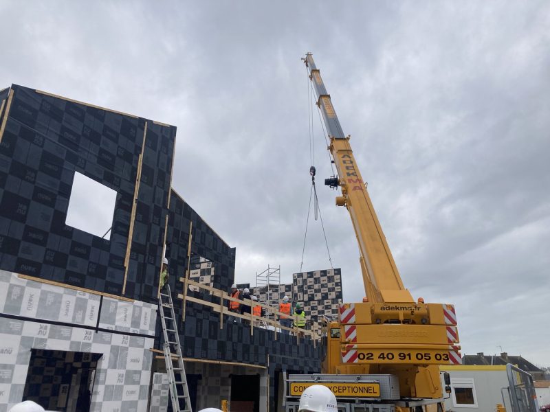 Construction d'une structure moderne en panneaux noirs avec grue jaune, chantier en cours sous ciel nuageux