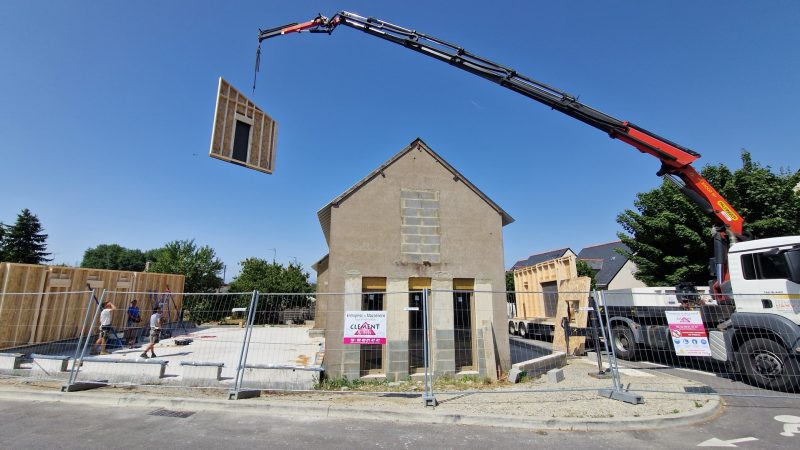 Grue levant un panneau préfabriqué à ossature bois au-dessus d'une maison en rénovation sur chantier