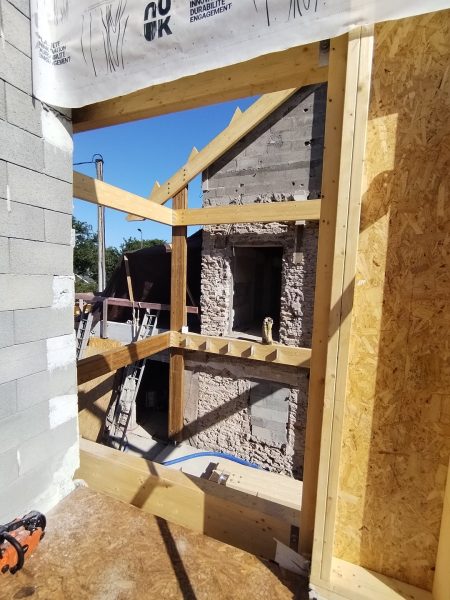 Construction d'une extension en bois avec ossature, murs en OSB et poutres apparentes, vue sur bâtiment existant en pierre