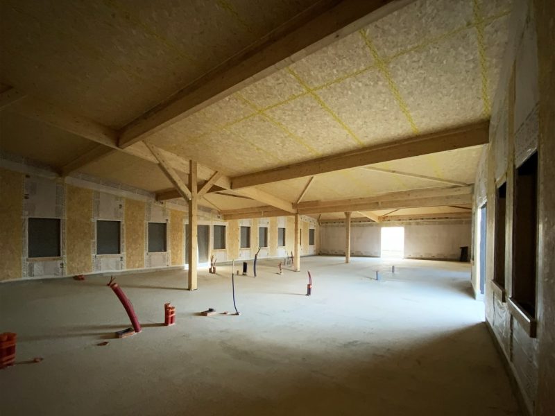 Espace intérieur en construction avec structure bois apparente, poteaux porteurs, isolation visible au plafond et ouvertures murales